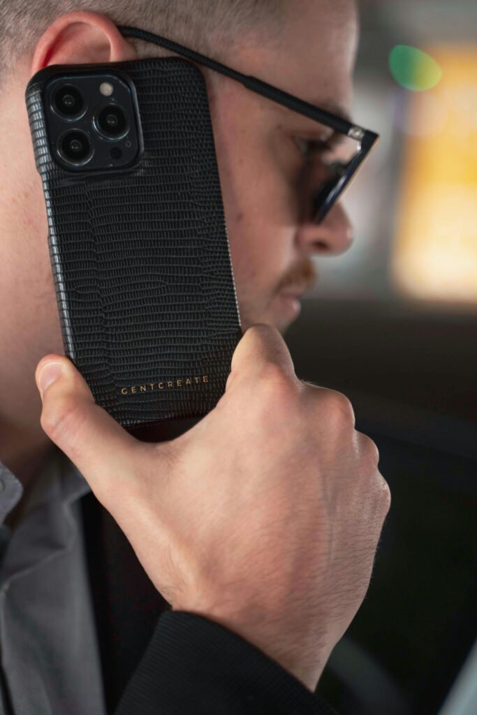 Stylish man with sunglasses holding luxury leather-clad iPhone. Modern elegance meets technology.